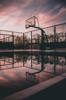 A tranquil view of a basketball court with reflections during sunset, creating a serene urban landscape.